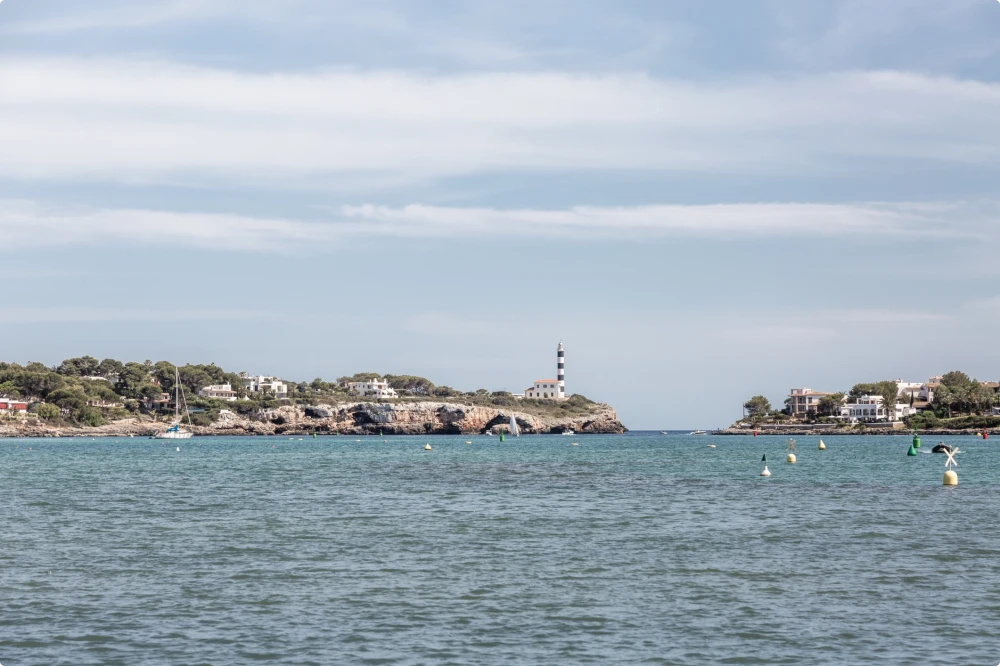 View of the iconic striped lighthouse and calm waters of the Porto Colom harbour